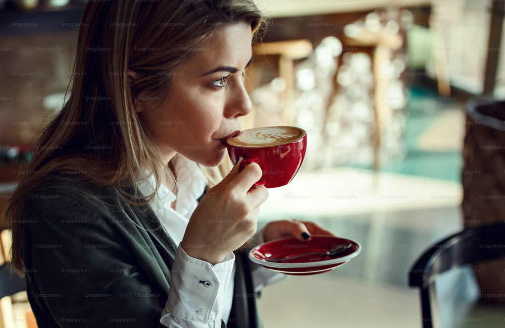 Joven empresaria pensativa disfrutando del sabor del café con leche mientras está sentada sola en un café.