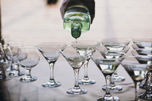 Waiter pouring martini in crystal glasses on table party at wedding reception. Martini row drinks at alcohol bar. Christmas and New Year feast. Celebrations and party concept.