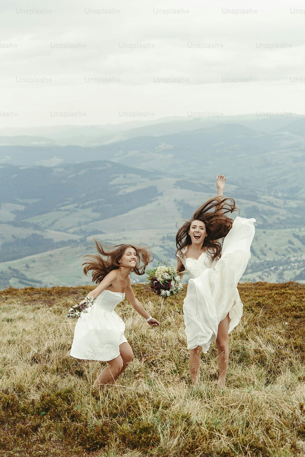 stylish bridesmaid and gorgeous bride having fun and jumping, boho wedding, luxury ceremony at mountains