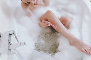 다리를 면도하는 동안 목욕을 하는 쾌활한 젊은 여자