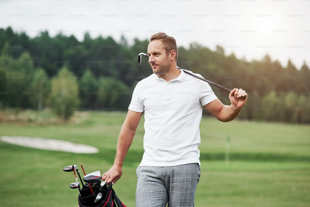 Portrait of walking golf player in the lawn and equipment in hands. Woods at background.
