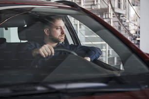 Olhar pensativo. Vista frontal do jovem empresário barbudo sentado em seu carro vermelho de luxo.