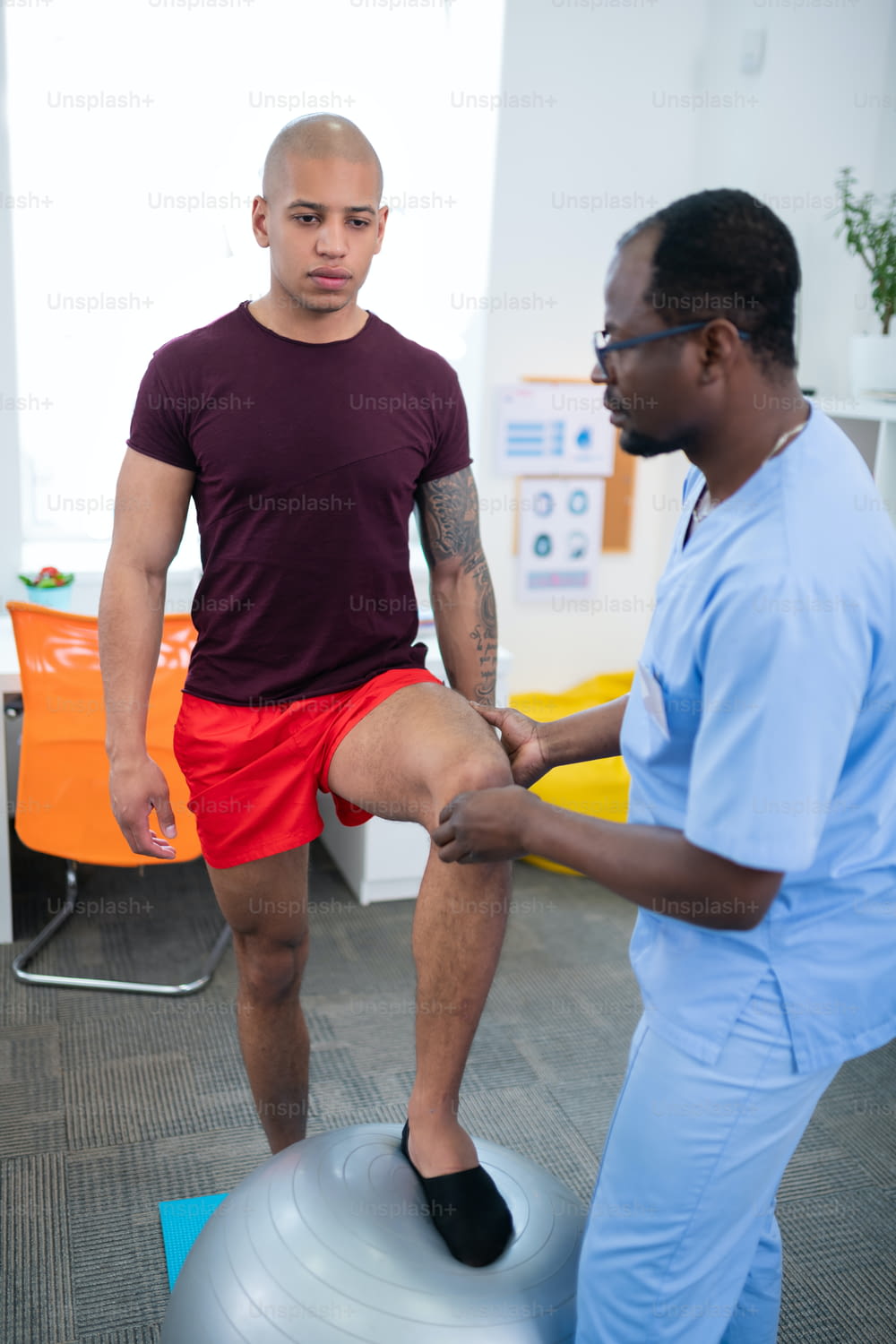 Examining knee. Therapist examining knee of bodybuilder standing near fit ball after serious injury