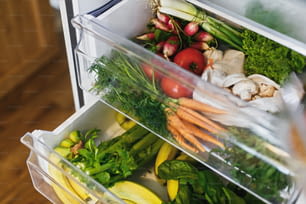 Épicerie zéro déchet dans le frigo. Légumes frais dans le tiroir ouvert du réfrigérateur. Carottes, tomates, champignons, bananes, salades, céleri, pommes, achats zéro déchet. Livraison d’épicerie