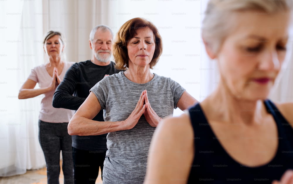 Groupe de personnes âgées actives faisant de l’exercice de yoga dans le club du centre communautaire.