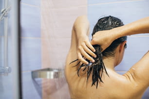 Junge glückliche Frau, die zu Hause oder im Hotelbadezimmer duscht. Schönes brünettes Mädchen, das sich die Haare wäscht und die Zeit zum Entspannen genießt. Körper- und Hauthygiene, Lifestyle-Konzept
