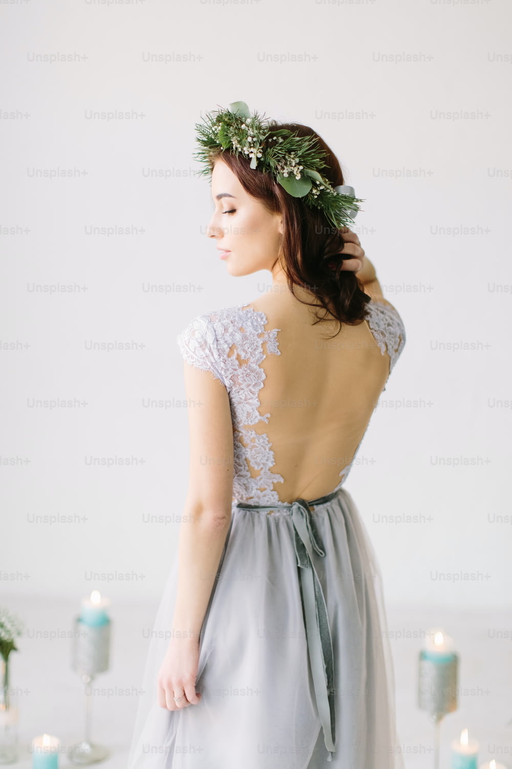 Beautiful young girl in a gray evening dress and a wreath of pine and eucalyptus on her head poses on the background of wedding scenery. Bridesmade poses in the studio before wedding ceremony.