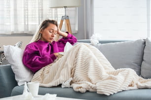 Mulher doente com dor de cabeça sentada sob o cobertor. Mulher doente com infecções sazonais, gripe, alergia deitada na cama. Mulher doente coberta com um cobertor deitada na cama com febre alta e uma gripe, descansando.