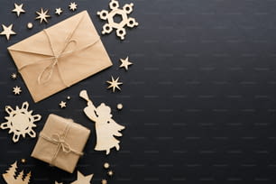 Décorations de Noël en bois, boîte cadeau, enveloppe en papier kraft avec lettre sur fond noir foncé. Maquette de carte de voeux de Noël. Composition minimale de style à plat, vue de dessus, espace de copie.
