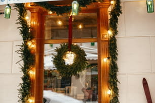 도시 거리의 휴일 시장에서 상점 앞 창문에 전나무 가지와 조명이 있는 세련된 크리스마스 화환. 텍스트를 위한 공간입니다. 소박한 장식. 크리스마스 거리 장식입니다.