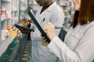 African Man Pharmacist using digital tablet to make an order in Distribution Company while his female colleague makes notes on clipboard. Work in Pharmacy. Drugstore Interior, Pharmaceutical Store.
