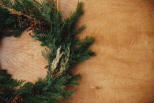 Natal rústico grinalda flat lay. Coroa de Natal rural criativa com ramos de abeto, bagas, pinhas e ervas sobre mesa de madeira. Espaço de cópia. Saudações das estações