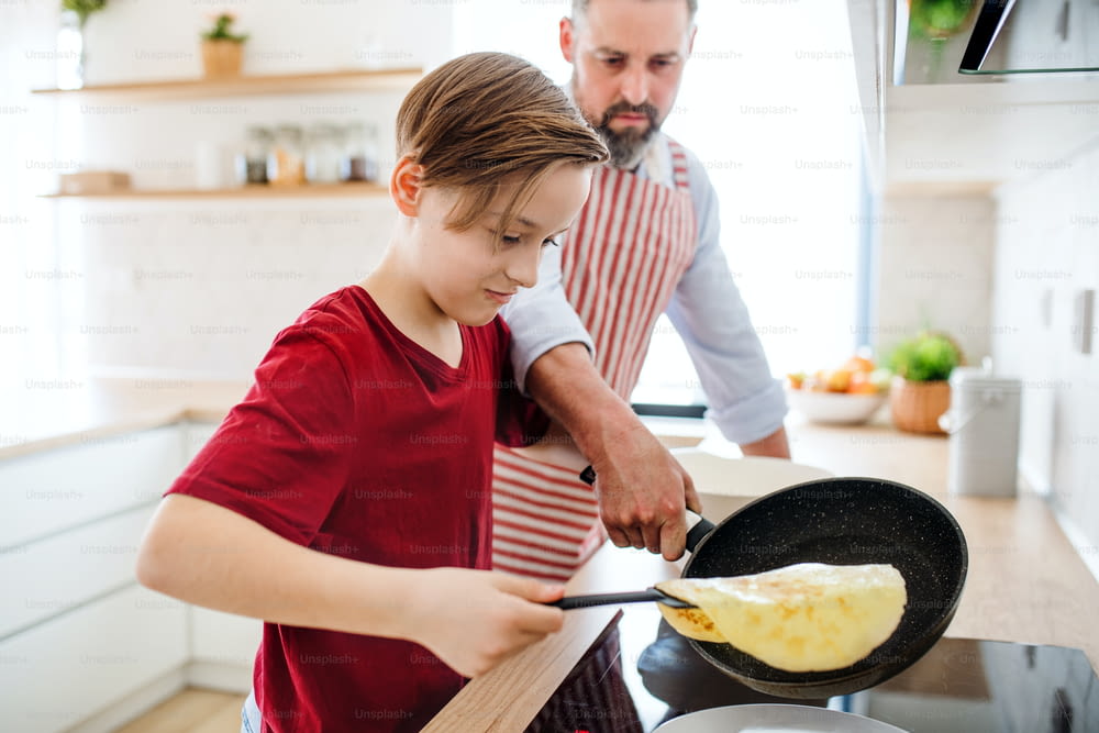 A small boy with father indoors in kitchen, learning how to make pancakes.
