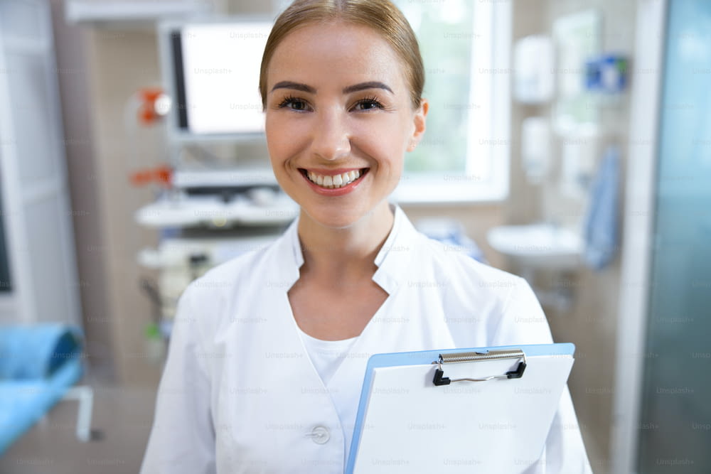 Delighted medical worker with clipboard is standing in modern office