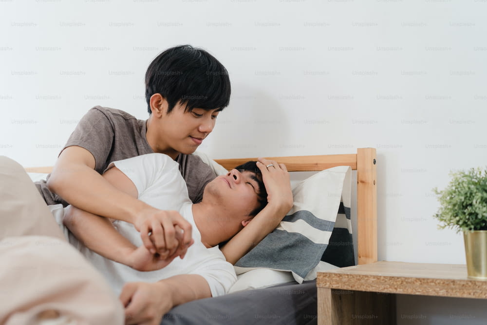 Casal gay asiático beija e abraça na cama em casa. Jovens asiáticos LGBTQ homens felizes relaxar descansar juntos passar o tempo romântico depois de acordar no quarto em casa no conceito da manhã.
