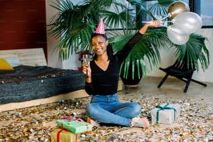 Birthday party, new year carnival. Young african smiling woman celebrating brightful event, . Sparkling confetti, having fun, dancing and drinking champagne