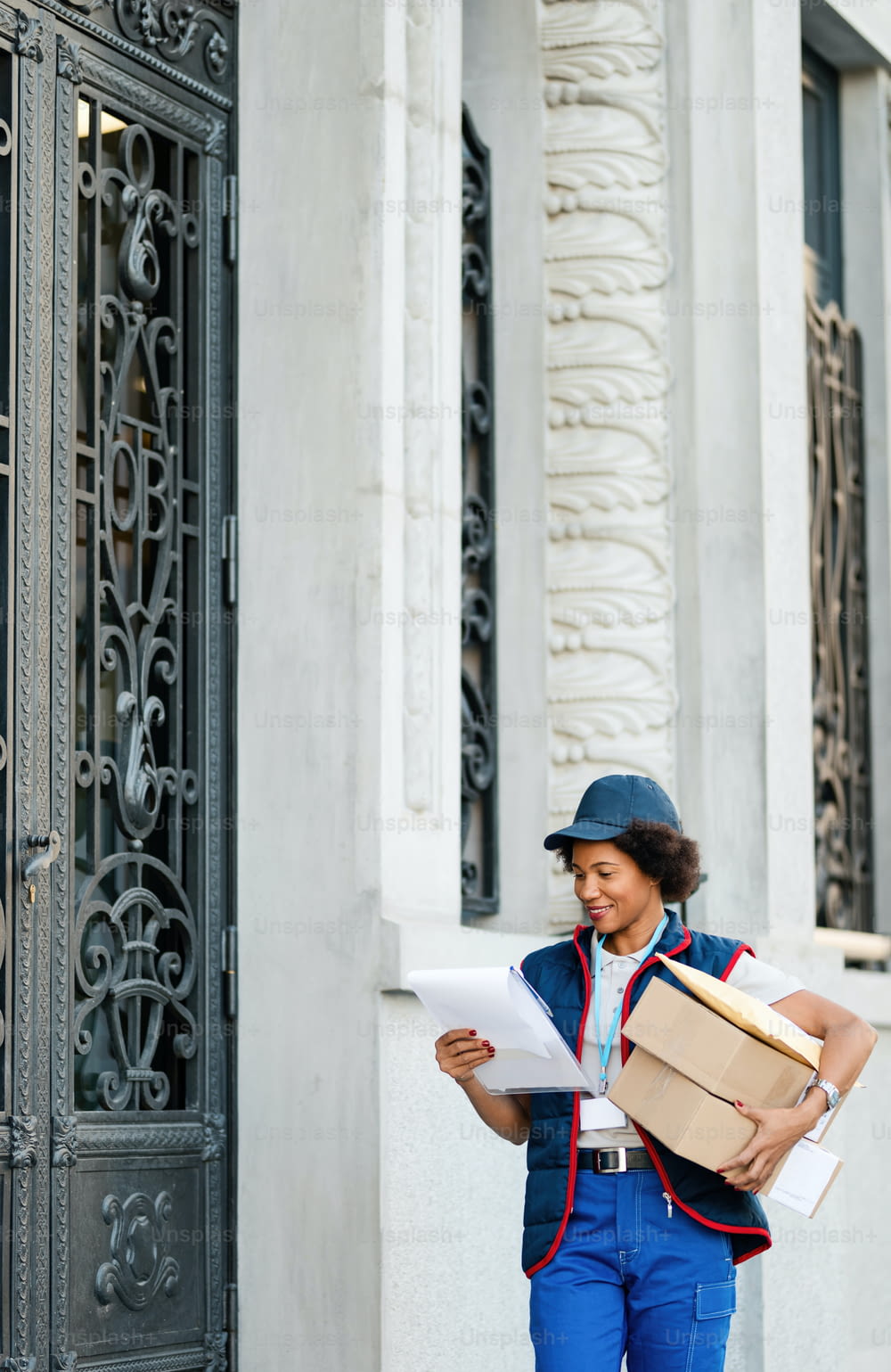 Smiling African American female courier delivering packages while reading address on the list in the city.
