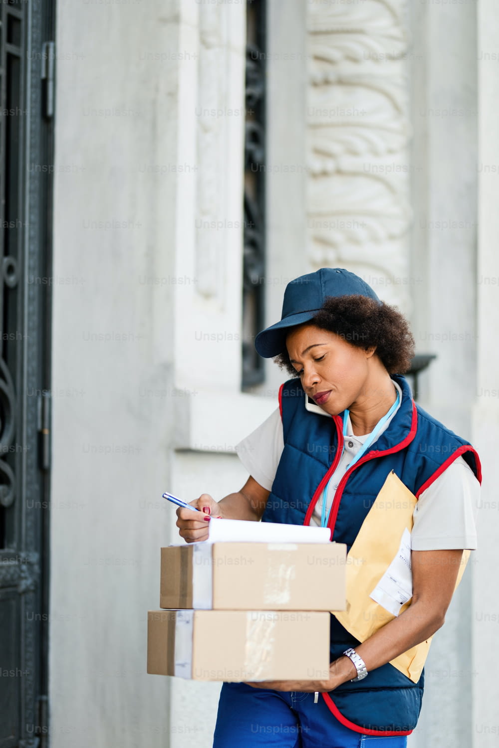 Black female courier taking notes while talking on the phone and making a delivery in the city.
