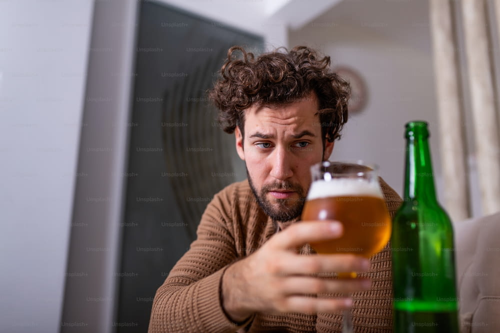 퇴근 후 소파에 앉아 차가운 맥주를 마시는 우울한 남자. 잔을 들고 있는 손, 혼자 집에 술을 마시는 남자. 알코올 중독, 알코올 중독 및 사람 개념