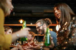 Un petit groupe de meilleurs amis debout dans un pub, buvant de la bière, discutant et s’amusant. Concentrez-vous sur le barman qui essuie le verre. Vie nocturne.