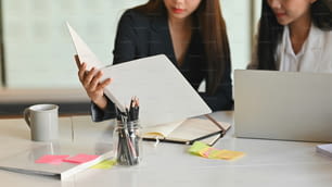 Primer plano de la joven empresaria segura de sí misma que muestra el archivo de documentos a su colega mientras está sentada en el escritorio de trabajo en la oficina moderna.