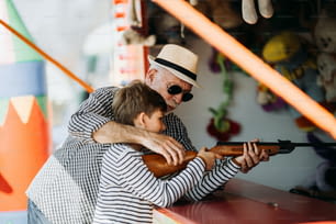 Avô e neto se divertindo e passando um tempo de boa qualidade juntos no parque de diversões. Garoto atirando com arma de ar enquanto o vovô o ajuda a ganhar o prêmio.