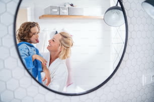 A reflection of mother and small daughter in mirror in bathroom indoors at home, making faces.
