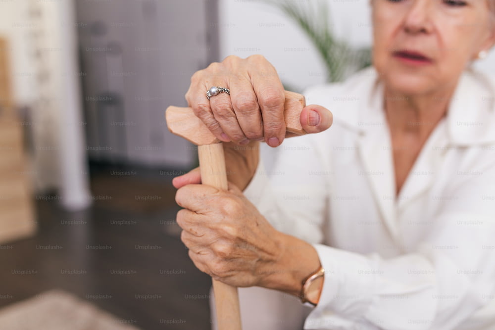 Mani di una vecchia con un bastone, signora anziana seduta sul divano con bastone da passeggio di legno. Scatto ritagliato di una donna anziana che tiene un bastone in una casa di riposo