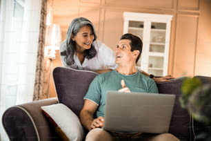 Waist up of happy couple in love using laptop while sitting in living room stock photo