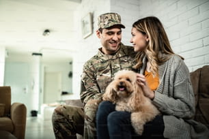 Soldado del ejército feliz y su esposa comunicándose mientras se relajan en casa con su perro.