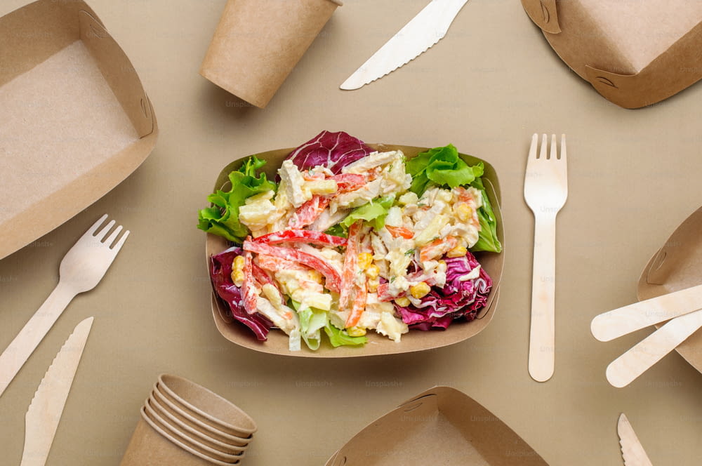 일회용 친환경 식품 포장. 베이지색 배경에 갈색 크래프트 종이 음식 용기에 담긴 야채 샐러드. 평면도, 플랫 레이.