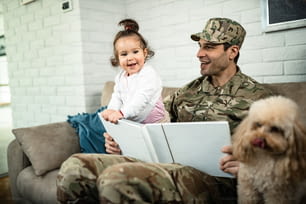 Padre militar feliz y su hija mirando el álbum de fotos y divirtiéndose en casa.
