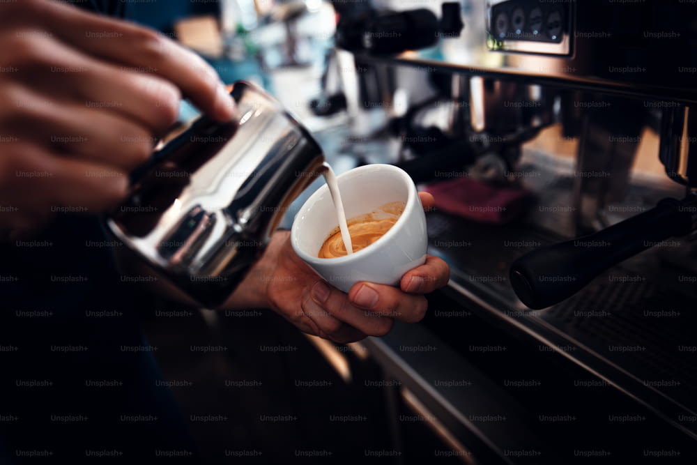 Close up of barista hands preparing cappuccino on espresso machine for customer in coffee shop.