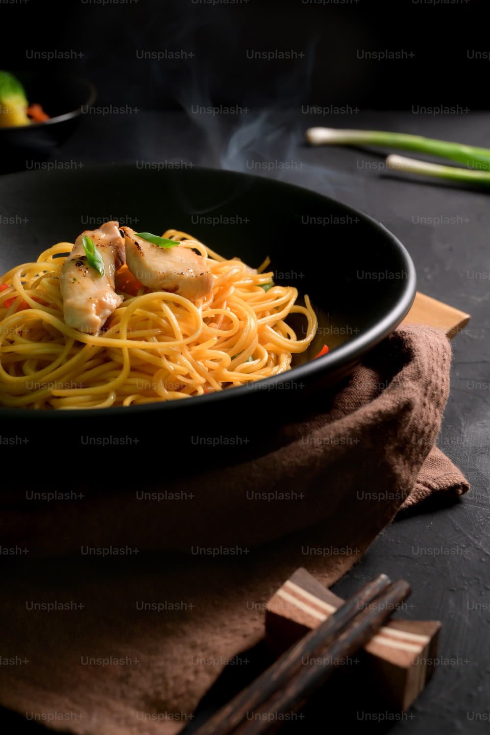 Cropped shot of Schezwan Noodles or Chow Mein in black bowl on black table with chopstick