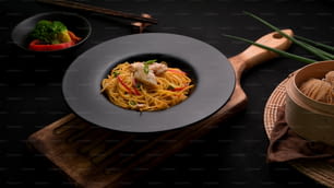 Cropped shot of Schezwan Noodles or Chow Mein with vegetable, chicken and chilli sauce served in black plate on wooden desk in Chinese restaurant