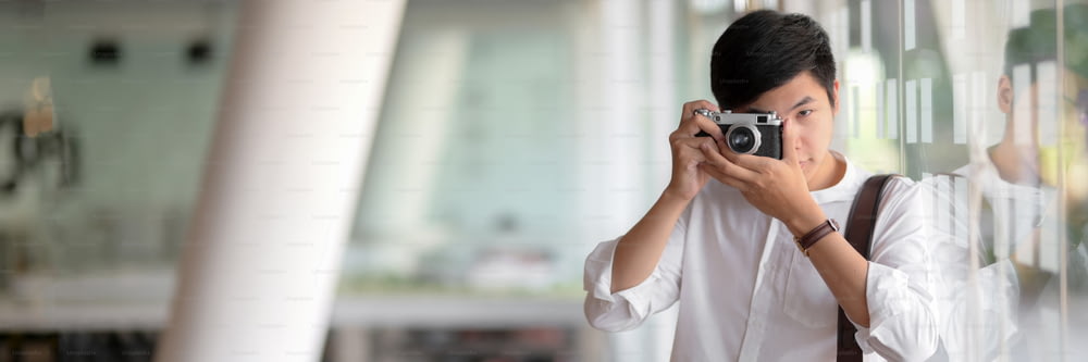 Cropped shot of young male photographer taking photo with digital camera while standing in glass wall office
