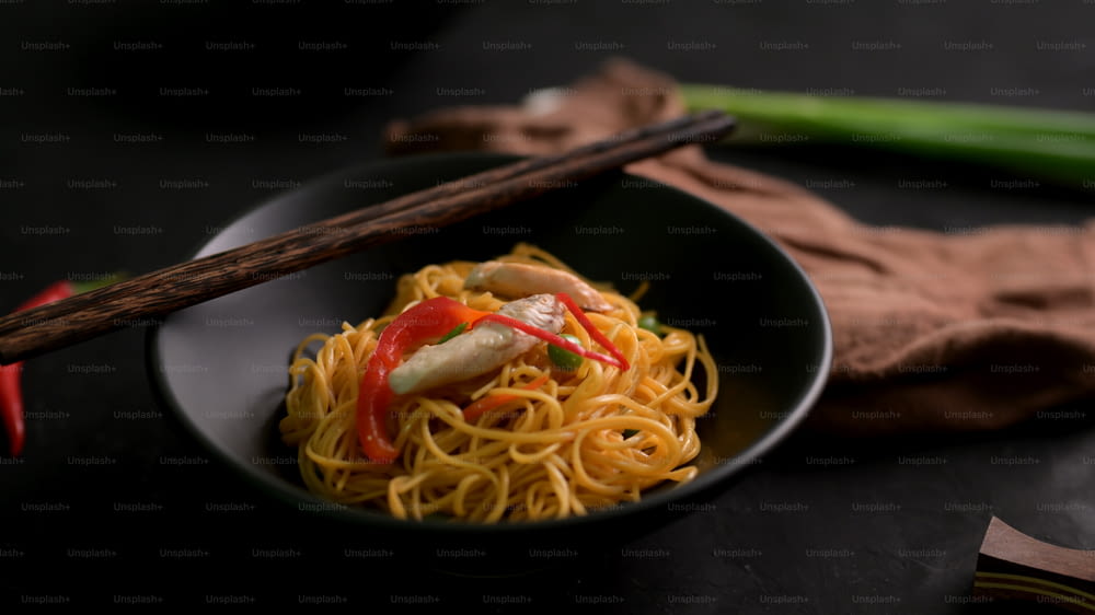 Cropped shot of Schezwan Noodles or Chow Mein in black bowl with chopsticks  on black table