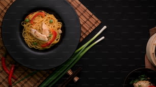 Overhead shot of Schezwan Noodles or Chow Mein with vegetable and chicken served in black plate on black table