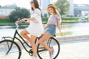Joyful young women riding a bicycle together. Best friends having fun on a bike at the river promenade in the city