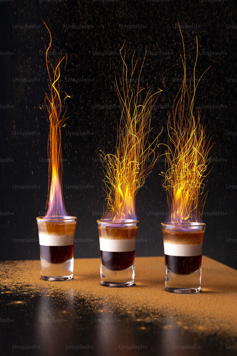 Three shots of burning B-52 cocktail placed on a bar counter, with sprinkling of cinnamon powder causing sparkes