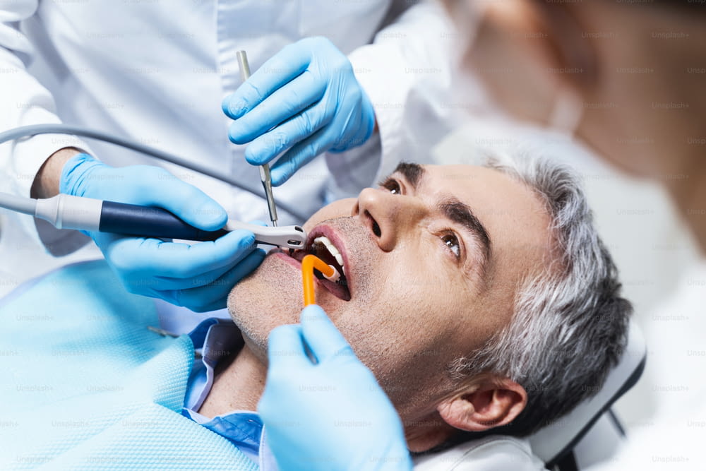 Male is lying in dental chair and being given root canal by dentist and assistant