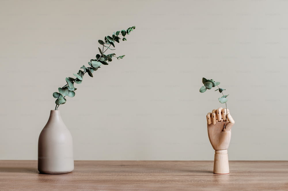 モダンな花瓶にユーカリの枝を乾燥させ、室内の木製のテーブルの上に木製の手を入れます。テキスト用の空白スペース。モダンな家のインテリアデザイン要素の背景。