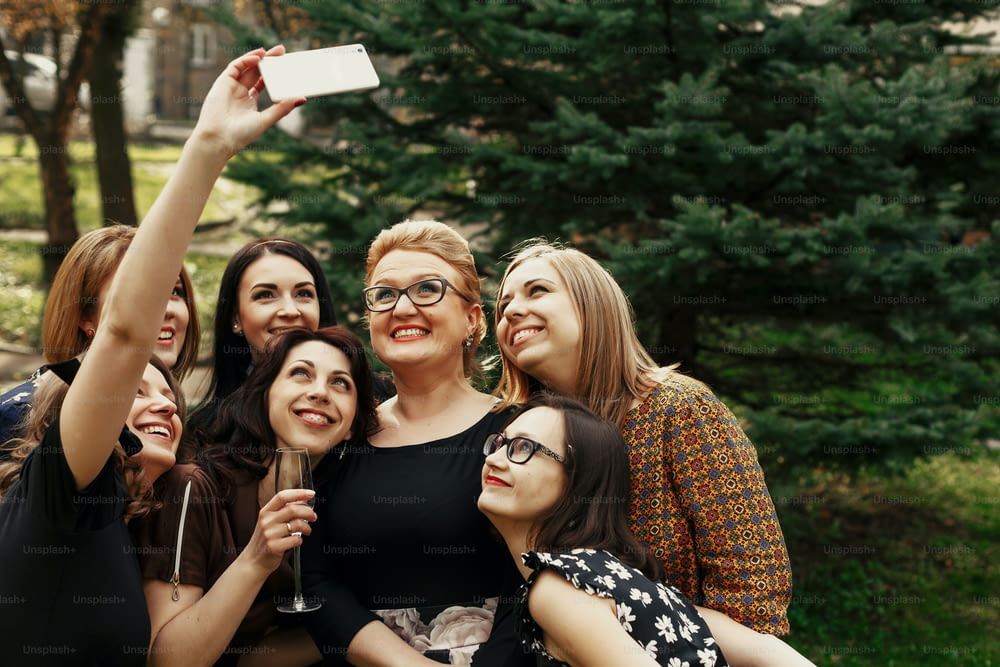 femmes élégantes et élégantes prenant un selfie drôle à la célébration ensoleillée dans le parc, concept de vie heureuse de luxe