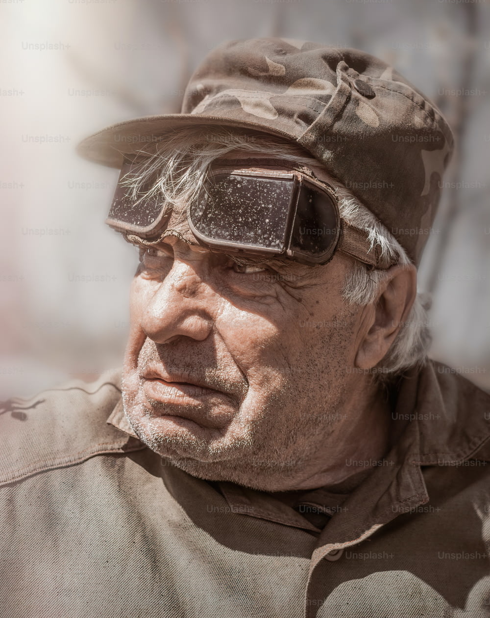 elderly white man of eighty years old in working uniform and old protective work glasses for welding. Wrinkled face and work clothes. Leisure in old age