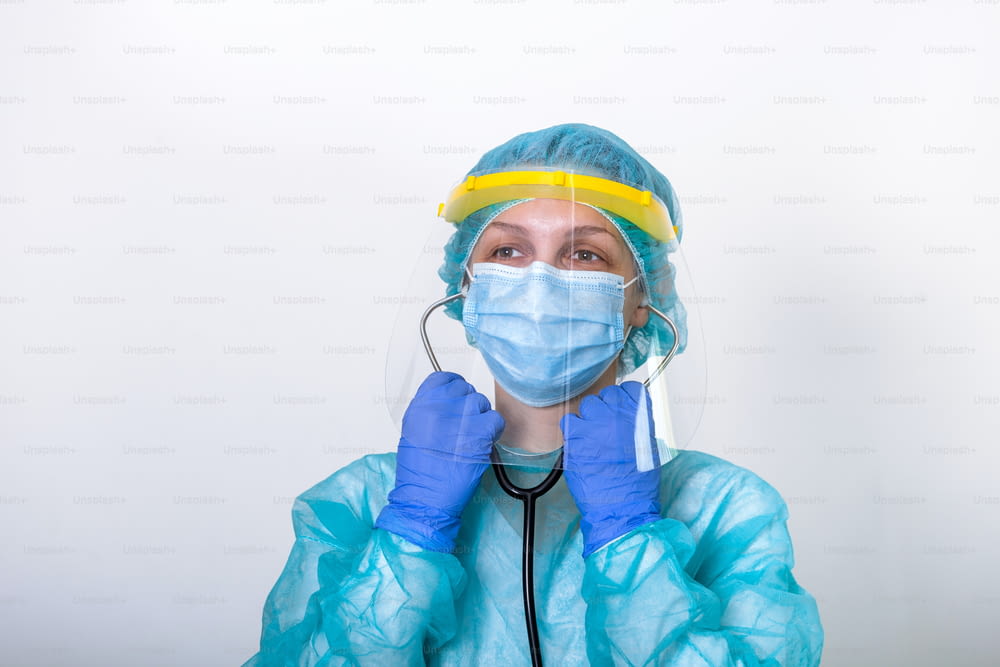 Médico, enfermeiro mostram como usar Traje de Proteção para Combater o Coronavírus Covid-19 com fundo branco isolado. trabalhadora médica em equipamento de proteção completo com escudo facial colocando seu estetoscópio