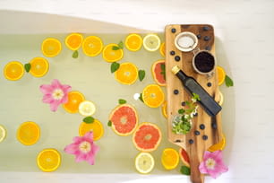 Relaxing bath with grapefruit, lemon and oranges slices. Beauty treatment products on wooden rustic board. Wellness concept