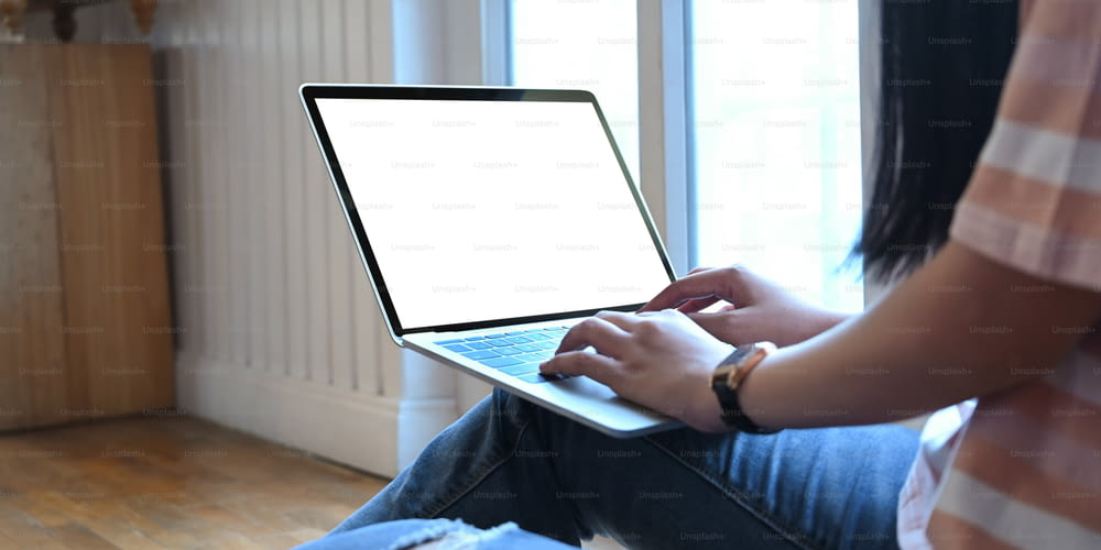 Cropped image of a woman is typing on a white blank screen computer laptop that putting on her lap.