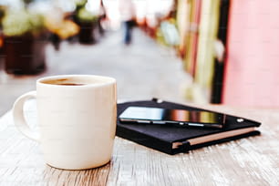 tazza di caffè e smart phone all'aperto su un tavolo al bar o al bar con sfondo sfocato