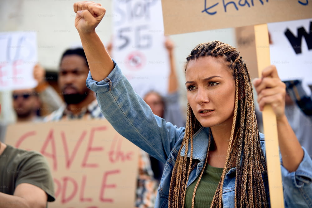도시 거리에서 활동가 그룹과 함께 항의하는 주먹을 든 젊은 백인 여성.