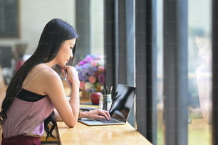 Eine junge Asiatin arbeitet mit einem schwarzen Computer-Laptop auf dem leeren Bildschirm an der Holztheke.